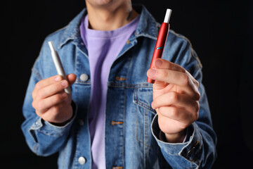 Young man with electronic cigarettes on black background, closeup