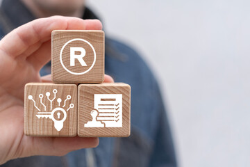 Man holding wooden blocks with icon sees sigr with letter: R. Registered trademark ( R ) copyright or patent concept. Trade mark protection.