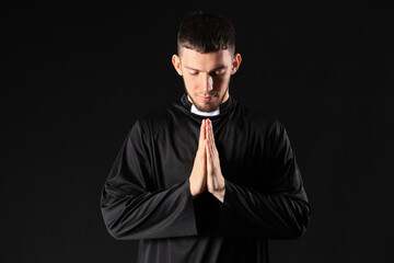 Young priest praying on black background