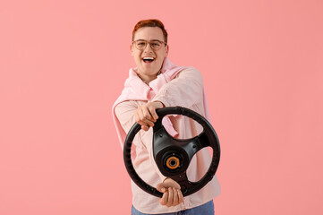 Happy young man in eyeglasses with steering wheel on pink background