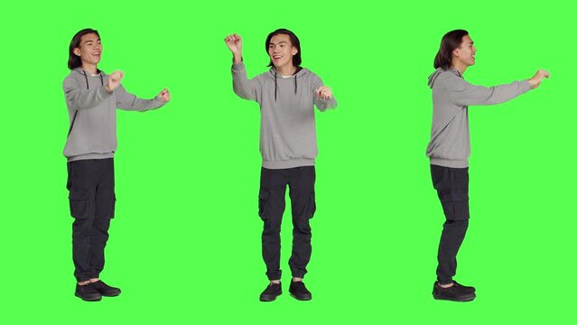 Asian man acting as choir director for musical show, moving hands like a choirmaster chief over greenscreen backdrop. Male person conducting band to sing, smiling choirmaster musician.