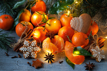 Tangerines mandarin fruit with cinnamon, gingerbread, cookies, anise, pine branches and a light garland on a wooden table. Christmas card.