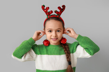 Cute little girl in reindeer horns with Christmas balls on grey background
