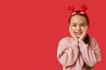 Cute little girl in reindeer horns on red background