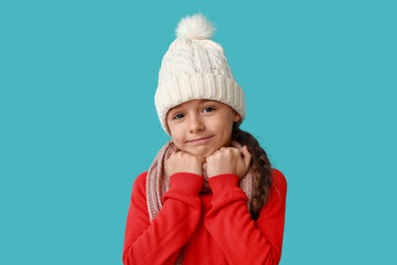 Cute little girl in warm hat and scarf on blue background