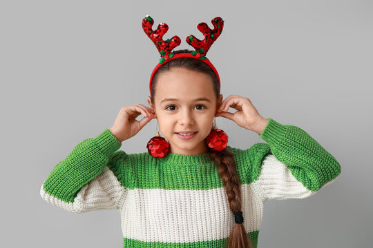 Cute little girl in reindeer horns with Christmas balls on grey background