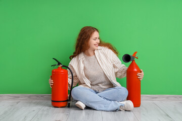 Young woman with fire extinguisher sitting near green wall