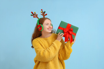 Young woman in reindeer horns with Christmas gift on blue background