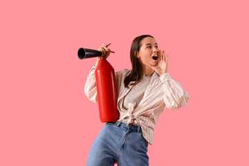Young woman with fire extinguisher shouting on pink background