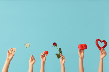Female hands with decorative hearts, red rose and gift box on blue background. Valentine's Day celebration