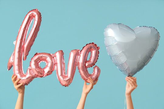 Female hands with air balloons in shape of word LOVE on blue background. Valentine's Day celebration