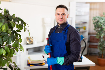 Male professional janitor dusting in modern office interior