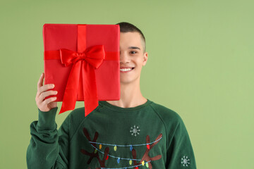 Teenage boy with Christmas gift box on green background
