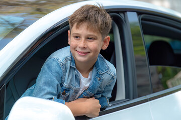 Excited and happy young little boy with smile on his face show up on car window while driving,...