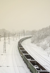 A long train of freight cars is moving along the railroad track. Railway landscape in winter after snowfall