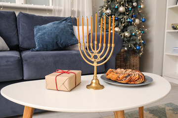 Coffee table with menorah, gift box and traditional babka in living room. Hanukkah celebration