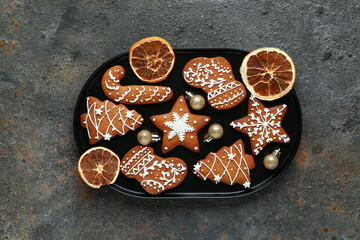Plate of Christmas gingerbread cookies with dried orange slices and balls on dark background