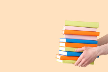 Hands holding stack of books on beige background