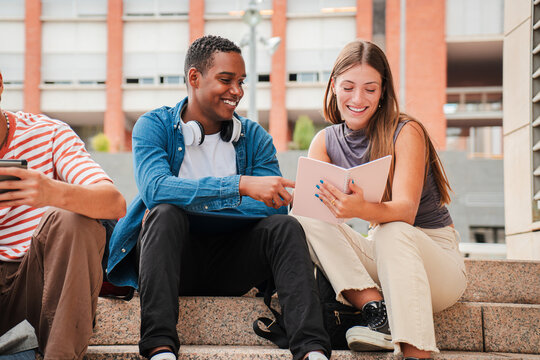 Two multiracial teenage studens learning together at university campus. African american schoolboy talking with a school girl about the homeworks. Young friends studying at highschool stairs. High
