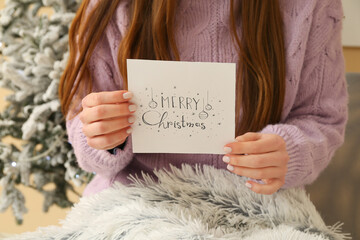 Young woman holding card with text MERRY CHRISTMAS, closeup
