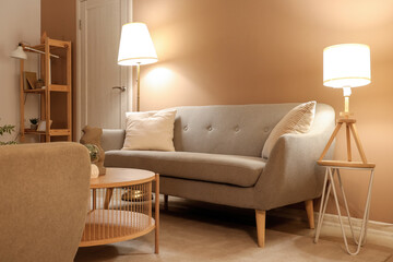 Interior of modern living room with grey sofa, coffee table and glowing lamps at evening