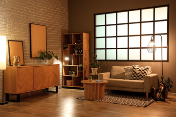 Interior of modern living room with grey sofa, coffee table, wooden cabinet and glowing lamps at...