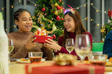 Group of Asian friends enjoying Christmas party for new year celebrate. Friends having fun together with dinner at home. men and women opening box gift and present together at home with Christmas tree