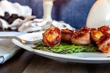 Candied bacon wrapped sea scallops over a bed of asparagus on fine China