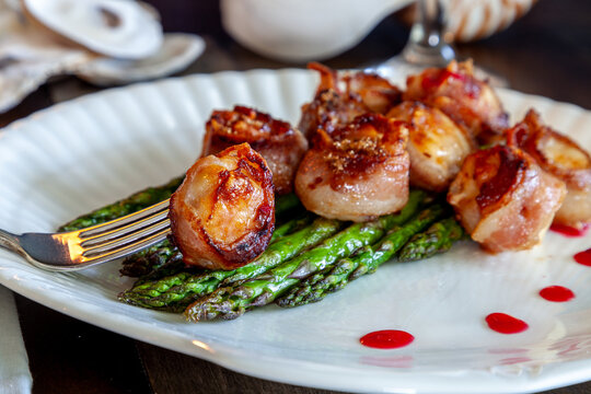 Candied bacon wrapped sea scallops over a bed of asparagus on fine China