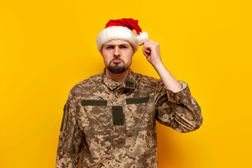 sad ukrainian soldier in pixel uniform and santa claus hat being offended on yellow isolated...