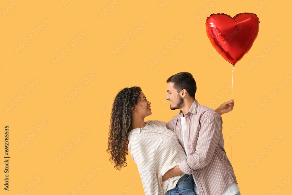 Wall mural young couple with air balloon in shape of heart for valentine's day on yellow background