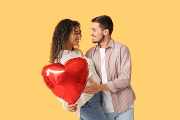 Young couple with air balloon in shape of heart for Valentine's day on yellow background
