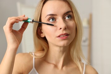 Fototapeta premium Beautiful woman applying mascara with brush indoors, closeup