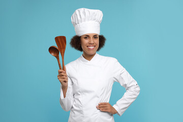 Naklejka premium Happy female chef in uniform holding spoon and spatula on light blue background