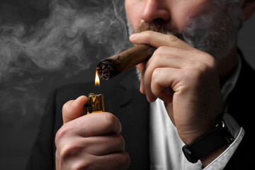 Bearded man lighting cigar on dark grey background, closeup
