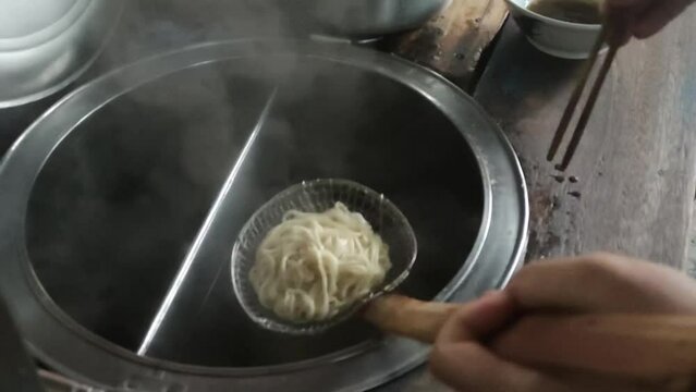 Making chicken noodles. View of a vendor of mie ayam bakso (meatball chicken noodles) preparing chicken noodles for a customer.