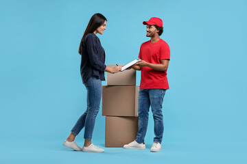 Smiling woman signing order receipt on light blue background. Courier delivery
