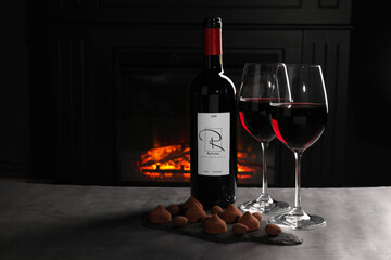 Red wine and chocolate truffles on gray table against fireplace, space for text