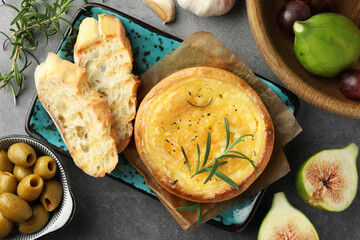 Tasty baked brie cheese and products on grey table, flat lay