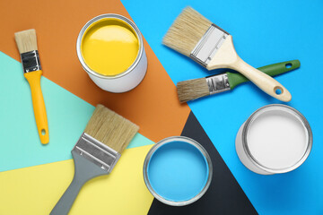 Cans of colorful paints and brushes on color background, flat lay