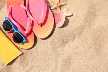 Fototapeta na wymiar Flip flops and other beach accessories on sand, flat lay. Space for text