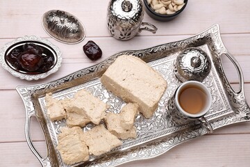 Pieces of tasty halva, tea and dates on light wooden table, above view