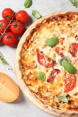 Tasty quiche with tomatoes, basil and cheese served on light table, flat lay