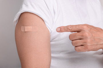 Man pointing at adhesive bandage after vaccination on light grey background, closeup