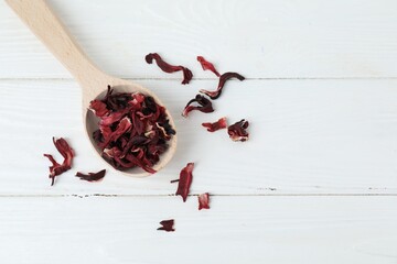 Hibiscus tea. Spoon with dried roselle calyces on white wooden table, top view. Space for text