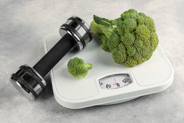 Healthy diet. Scale, broccoli and dumbbell on grey table