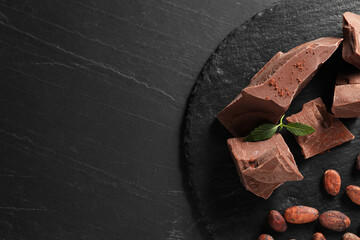 Pieces of tasty milk chocolate, cocoa beans, powder and mint on grey textured table, top view....