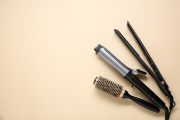 Curling iron, hair straightener and round brush on beige background, flat lay. Space for text