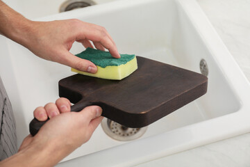 Man washing dark wooden cutting board at sink in kitchen, closeup