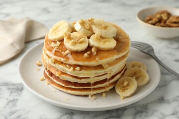 Delicious pancakes with bananas, walnuts and honey on white marble table, closeup
